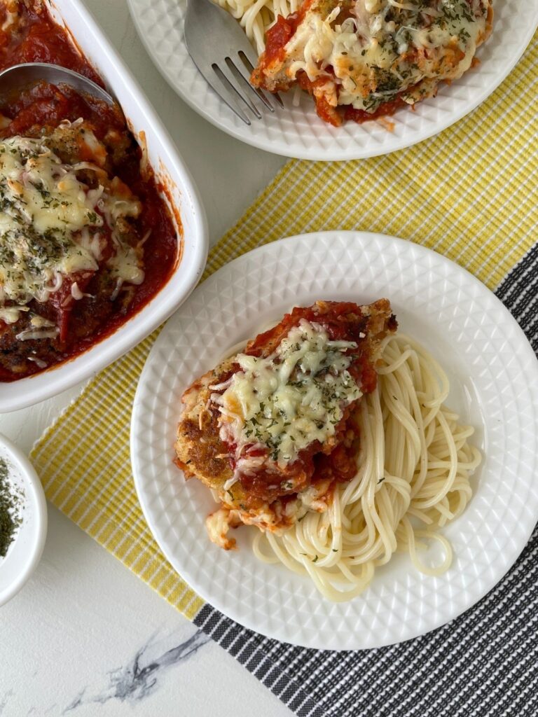 Chicken Cutlet Parmesan served with spaghetti on white plate.